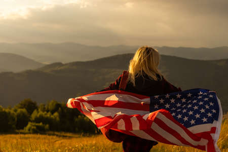 Woman holding USA flag on top of mountain and enjoys the view of the autumn rocks hills. Celebrating Independence Day of America.の写真素材