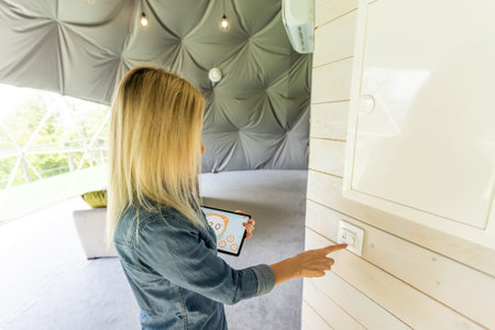 Young woman controlling temperature with smart phone and digital touch screen panel. Concept of...