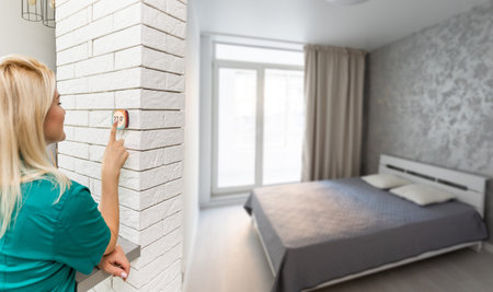 Woman controlling smart home devices using a digital tablet with launched application in the white...