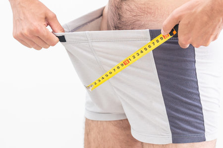 A man questioningly holds a measuring tape to his underpants.
