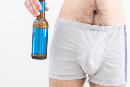 a man in underwear is holding a bottle of beerの写真素材