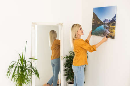 Canvas print with gallery wrap. Woman hangs photography on white wall. Hands holding photo canvas printの写真素材