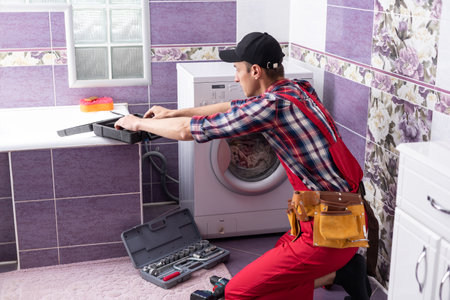 young serviceman checks broken washing machine loader on floor in room closeupの写真素材