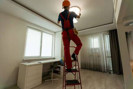 Worker installing lamp on stretch ceiling indoors. Space for textの写真素材