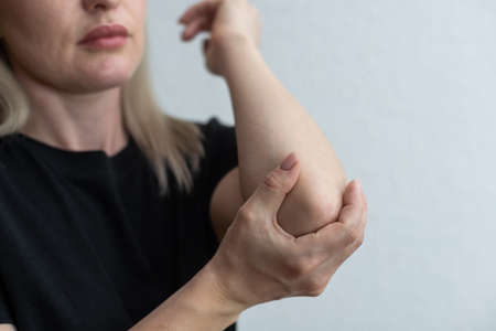 women elbow pain, holding hand to spot of elbow pain. Arm pain and injury conceptの写真素材