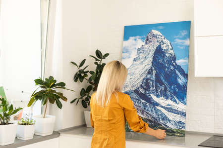 Modern Home Interior And Domestic Decor. Smiling young woman hanging painting, putting photo picture frame on the wall. Casual lady taking care of coziness in her new stylish apartment, profileの写真素材