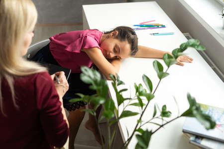 Professional female child psychologist working with a little preschool girl in a bright office. Woman makes notes about the condition of the girl on paper. Childrens mental therapy.の写真素材