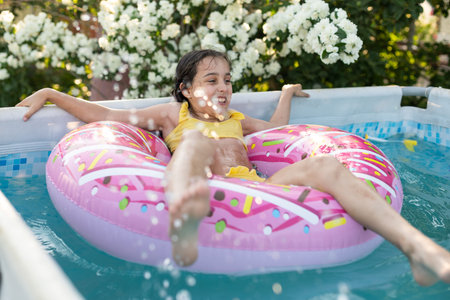 Happy little girl playing with colorful inflatable ring in outdoor swimming pool on hot summer day....