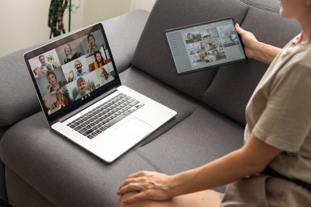 Young woman enjoying video conversation via laptop with eldery mother while sitting on sofa during...