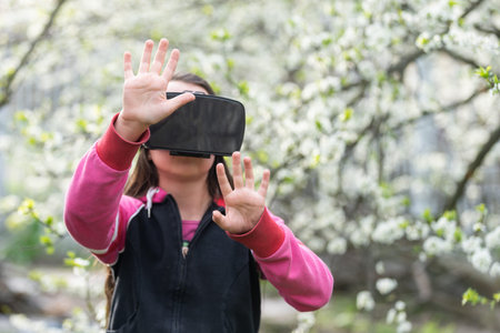 Full body little girl excited and entertained, playing with virtual reality glasses, exploring a...