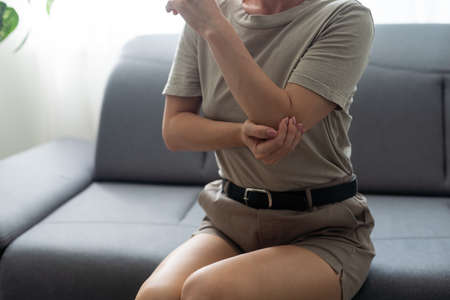 Females elbow pain. Arm pain and injury concept. Closeup side profile woman with painful elbow. Woman with elbow complaintsの写真素材