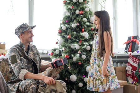 Soldier in uniform decorating Christmas tree with his daughter. An off duty military man spending Christmas holiday with his family at homeの写真素材