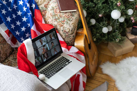 Online party with loved ones from USA. Celebrating Christmas video chat. Virtual party via video messenger. Americans new year are video chatting. New Year gifts and flag of America next to computerの写真素材