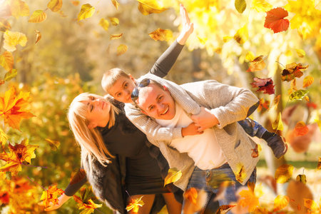 family, childhood, season and people concept - happy family playing with autumn leaves in park