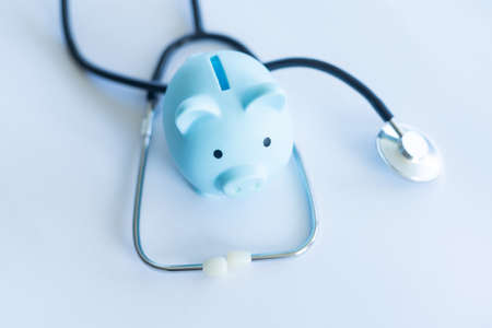 Piggy bank with stethoscope isolated on light blue background with copy space. Health care financial checkup or saving for medical insurance costs conceptの写真素材