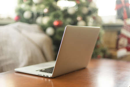 Laptop with empty screen on wooden table, blur Christmas tree and gifts on background.の写真素材