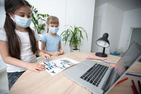 two little child girl studying online and working on laptop in wearing face maskの写真素材