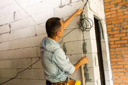 repairman in overalls wearing tool belt standing in building, renovation in the officeの写真素材
