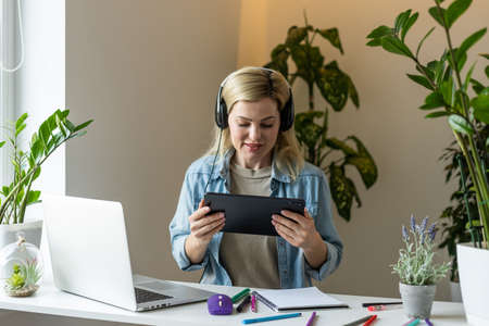 Image of young pleased happy cheerful cute beautiful business woman sit indoors in office using laptop computer listening music with earphonesの写真素材