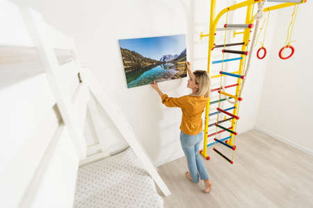 Canvas print with gallery wrap. Woman hangs photography on white wall. Hands holding photo canvas printの写真素材