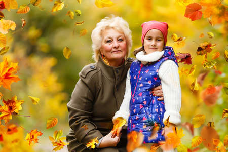 Granddaughter and grandmother hugging while sitting on a bench in the autumn forestの写真素材