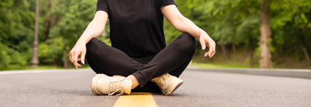 Joyful young lady in casual clothes walking along asphalt road in countryside, hitchhiking for ride outdoors. Lovely millennial woman traveling alone by autostopの写真素材