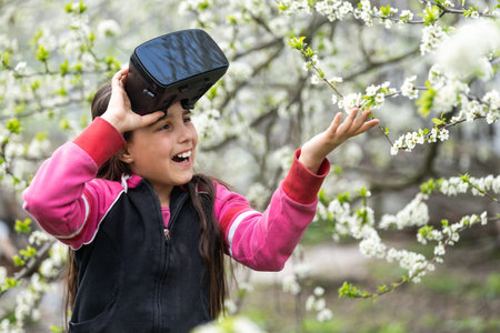 Full body little girl excited and entertained, playing with virtual reality glasses, exploring a...