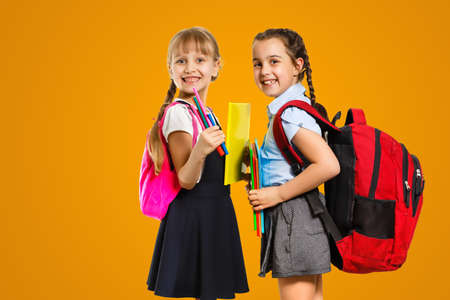 Education Concept. Set portrait of diverse schoolchildren holding stack of academic books and wearing backpack, yellow orange color studio backgroundの写真素材