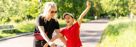 Beautiful and happy young mother teaching her daughter to ride a bicycle. Both smiling, summer park in background.の写真素材
