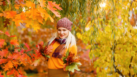 Portrait of cheerful young woman with autumn leafs in front of foliage making selfieの写真素材