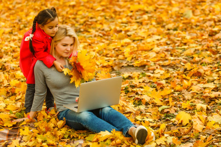 Urban woman and daughter with laptop in park. slim hipster woman in jeans using notebook. freelancer using communication technology remote work and eco-friendly lifestyle.の写真素材