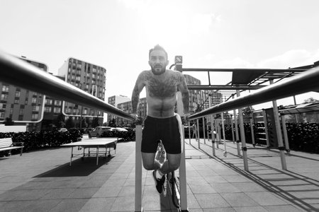 The young guy trains in the park on the street exercise machine