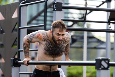 Muscular handsome man is training upper body on machines on street sports ground in city centre.