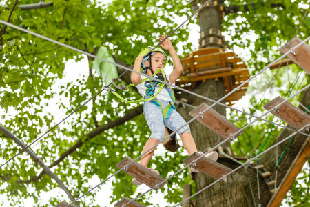 Happy school girl enjoying activity in a climbing adventure park on a summer day