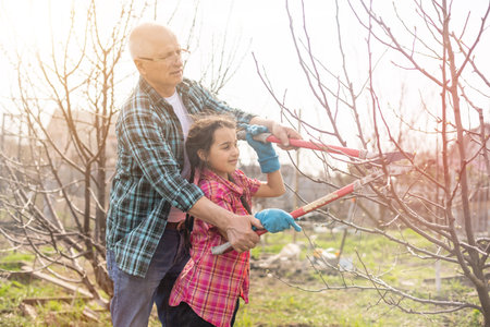 A small girl with grandfather outside in spring nature, having fun. gardening