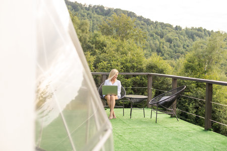 Hipster girl working with a laptop at home office in a glamping in the mountains with great views.