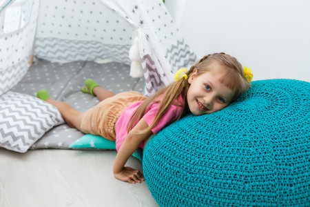 little girl on a childrens ottoman near a wigwamの写真素材