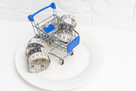 measure tape and mini shopping cart in white plateの写真素材