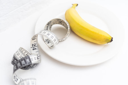 Measuring tape with banana on the plate. Healthy eating and diet concept.