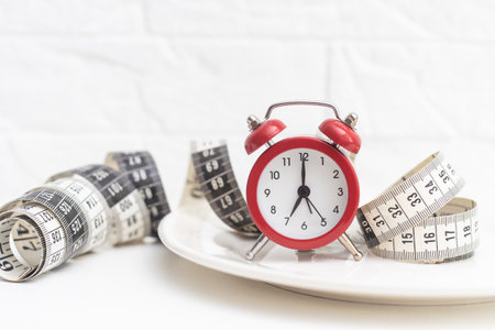 Time to lose weight concept. Red alarm clock with white plate and measuring tape close-up.の写真素材