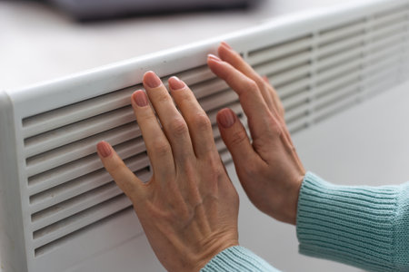 Womans hand on a white radiator. Heating season. Energy crisis. Cold batteries. Central heatingの写真素材