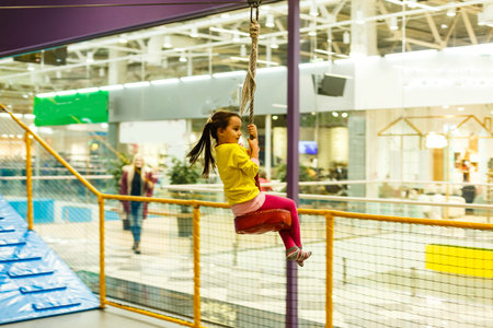 Adorable Little girl laughing happily, riding upside down on a bungee swing on the playground in...