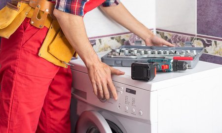 Young handyman fixing washing machine, closeup. Laundry day.の写真素材