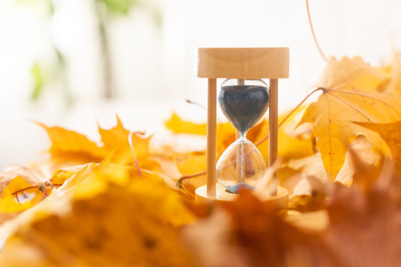 Hourglass and a yellow maple leaf on a dry autumn leafs
