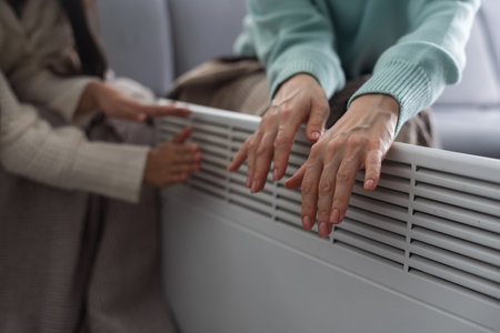 Mother and child warming hands near electric heater at home, closeup.の写真素材