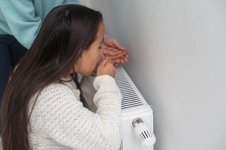 Child warming hands on heating radiator near white wall, closeupの写真素材