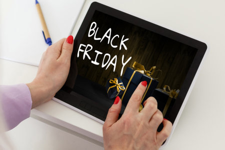 Black Friday sale concept. Tablet pad with sign Black Friday on screen, shopping bag, gift box over black backgroundの写真素材