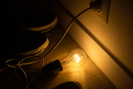 Single lightbulb hanging from a wire in a dark room with a warm glow.の写真素材