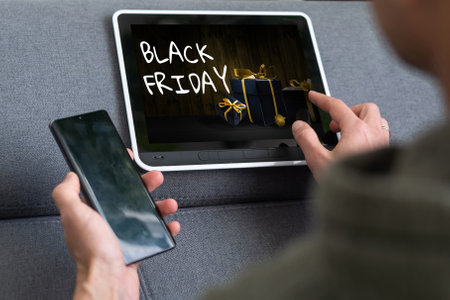 Black Friday sale concept. Tablet pad with sign Black Friday on screen, shopping bag, gift box over black backgroundの写真素材