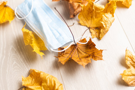 Surgical mask in pile of dry autumn leaves, flat lay top view covid-19 concept.の写真素材